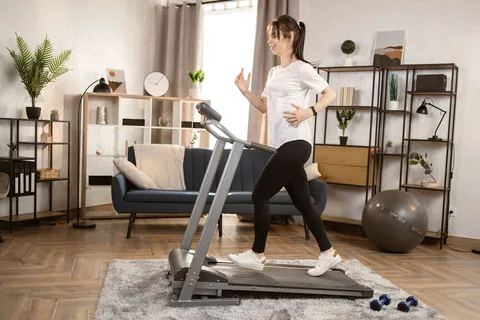 Jeune femme en train de courir sur un tapis de course dans son salon