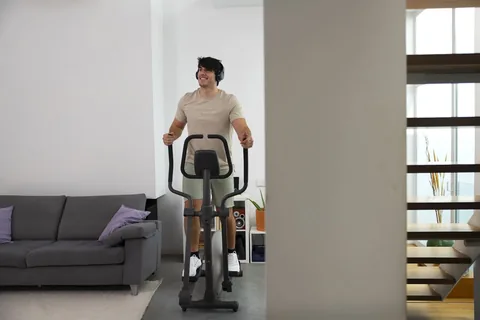 Jeune homme en train de faire du vélo elliptique dans son salon