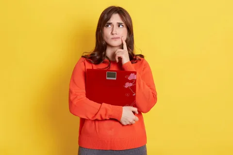 comment perdre du poids Femme qui s'interroge tout en tenant une balance dans les bras