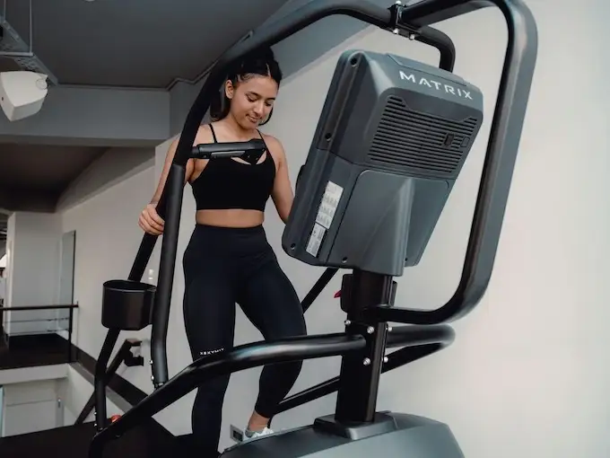 Femme s’entraînant sur un stepper Matrix en salle de sport, tenue noire, vue rapprochée de la console et des poignées.