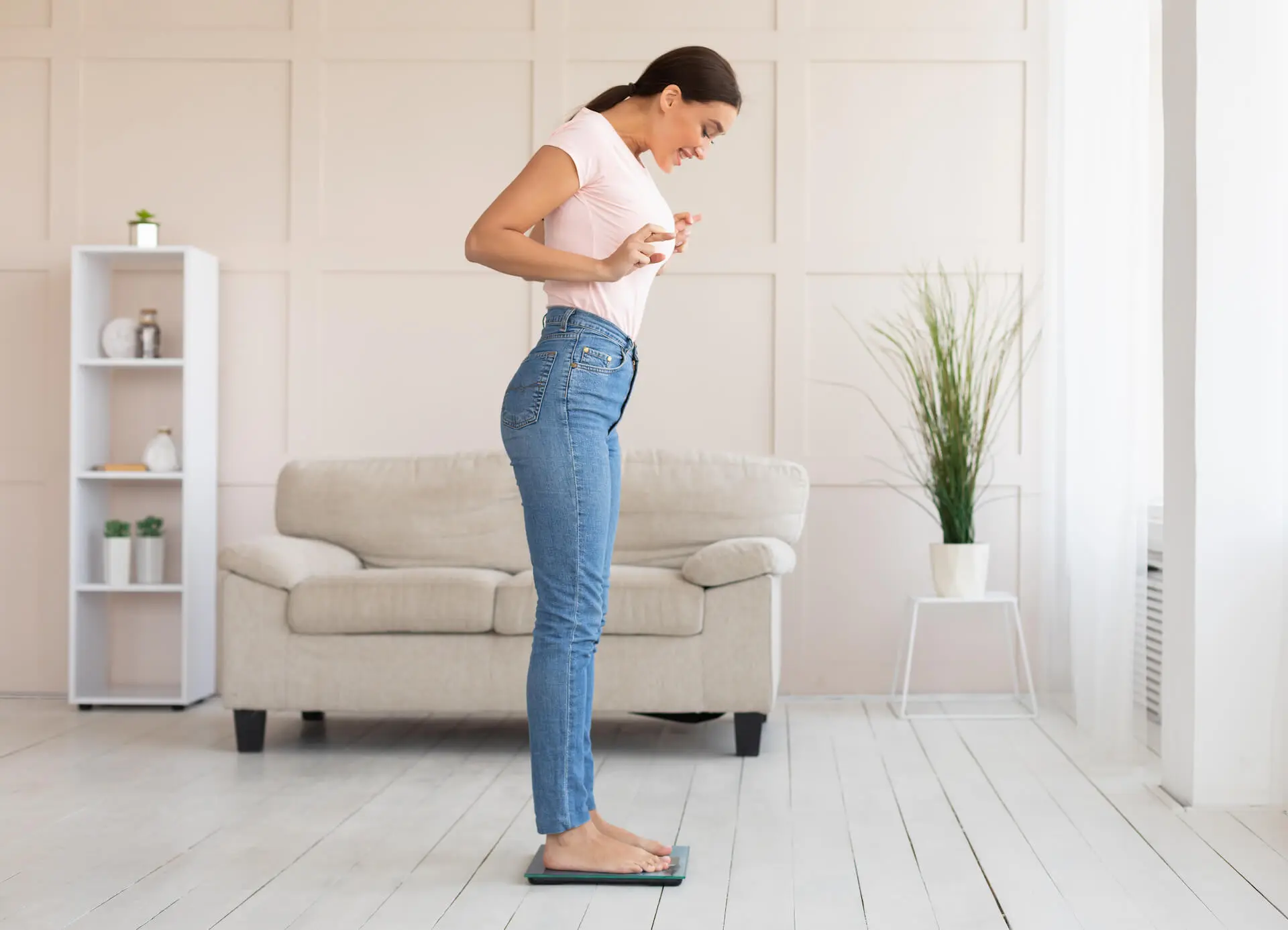 Femme en jean et T-shirt blanc se tenant sur une balance pour vérifier sa perte de poids