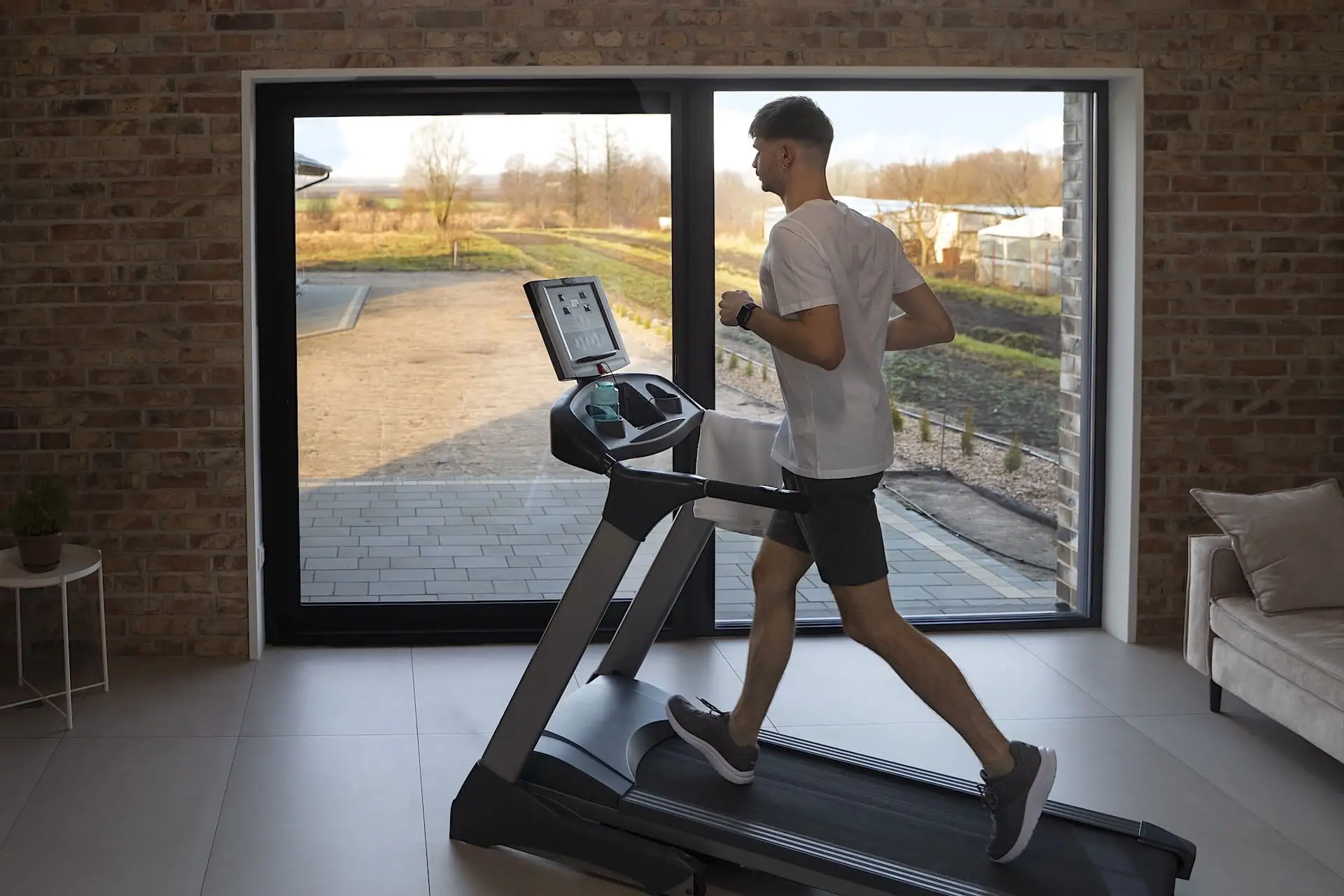 Bienfaits du tapis de course Jeune homme courant sur un tapis de course devant une baie vitrée